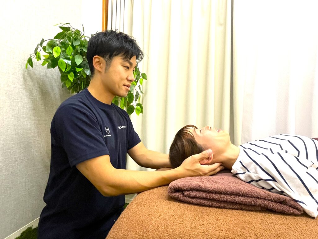 仰向けの状態で首まわりに手を当て、呼吸が深く入るように整えている様子